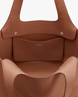 Close-up of a leather handbag with exterior pocket and top handles.