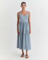 Woman standing in a dress and sandals, facing forward.
