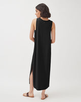 Woman standing in a long dress with a side slit, viewed from behind.