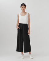 Woman standing in sleeveless top and loose pants, wearing sneakers.