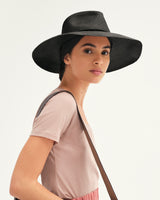 Woman wearing a wide-brimmed hat and carrying a shoulder bag looking over her shoulder.