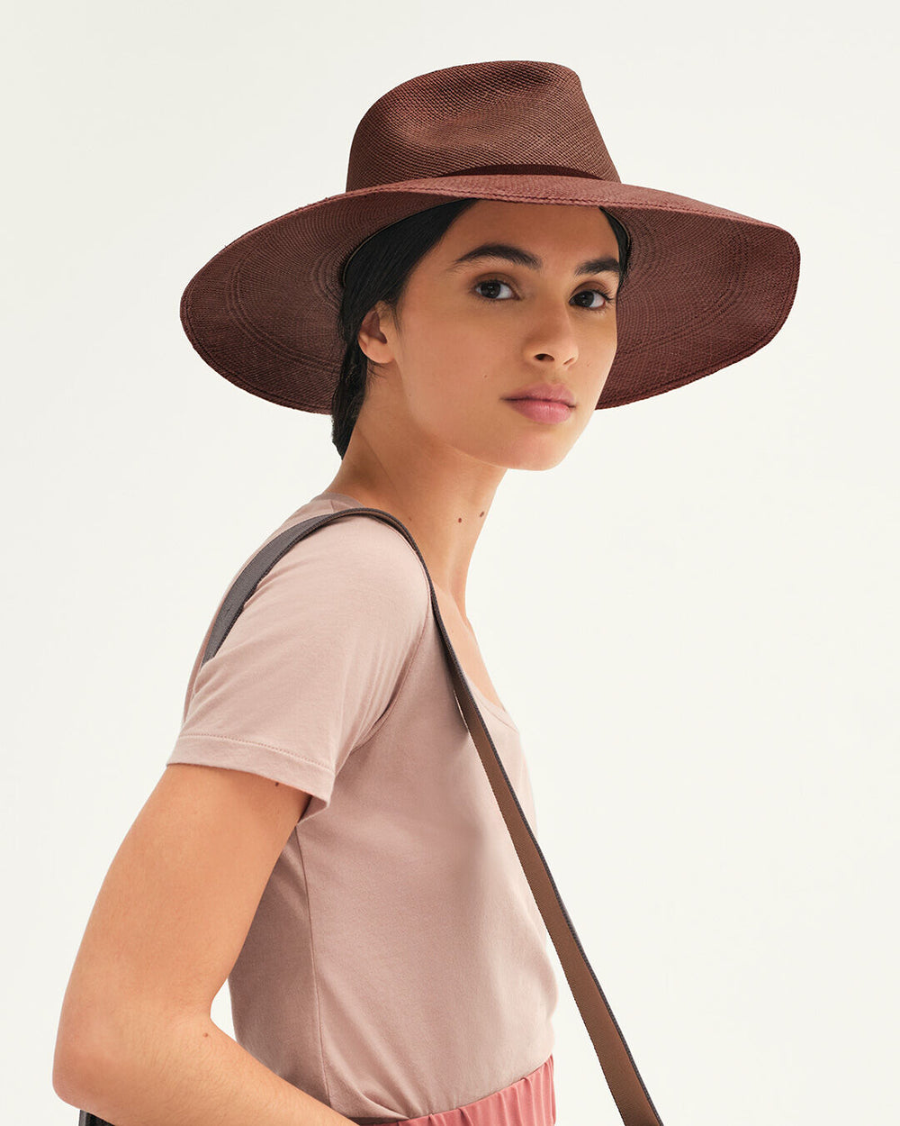 Woman wearing a wide-brimmed hat and a shoulder bag looking at the camera.