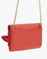 Purse with chain strap and front flap hanging against plain background.