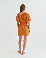 Woman standing with her back to the camera wearing a short jumpsuit.