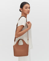 Woman standing sideways holding a handbag over her shoulder.