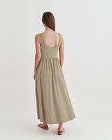 Woman standing facing away, wearing a long dress and sandals.