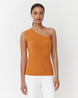 Woman in one-shoulder top and white pants standing against a white background.