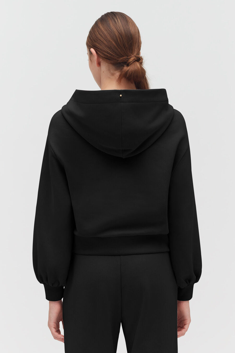 Person seen from behind wearing a hooded top and pants.