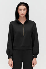 Woman in a hoodie standing with a neutral expression.