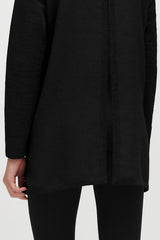 Person wearing a long-sleeved top and pants, close-up on torso.