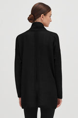 Woman seen from behind, wearing a high-neck jacket with her hair in a bun.