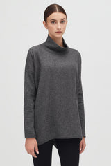 Woman in a turtleneck top and leggings standing against a plain background.