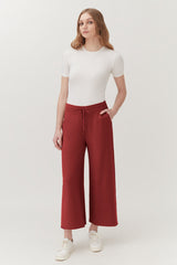 Woman in a short sleeve top and wide-leg trousers standing in a studio.