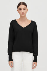 Woman standing with hands slightly apart, wearing a V-neck sweater and pants.