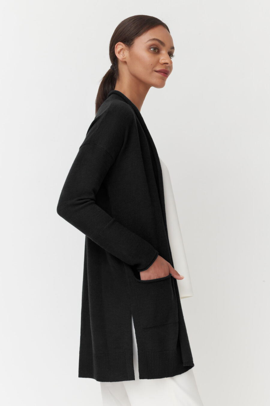 Single-Origin Cashmere Long Cardigan Woman standing with her hands in her jacket pockets, looking over her shoulder.