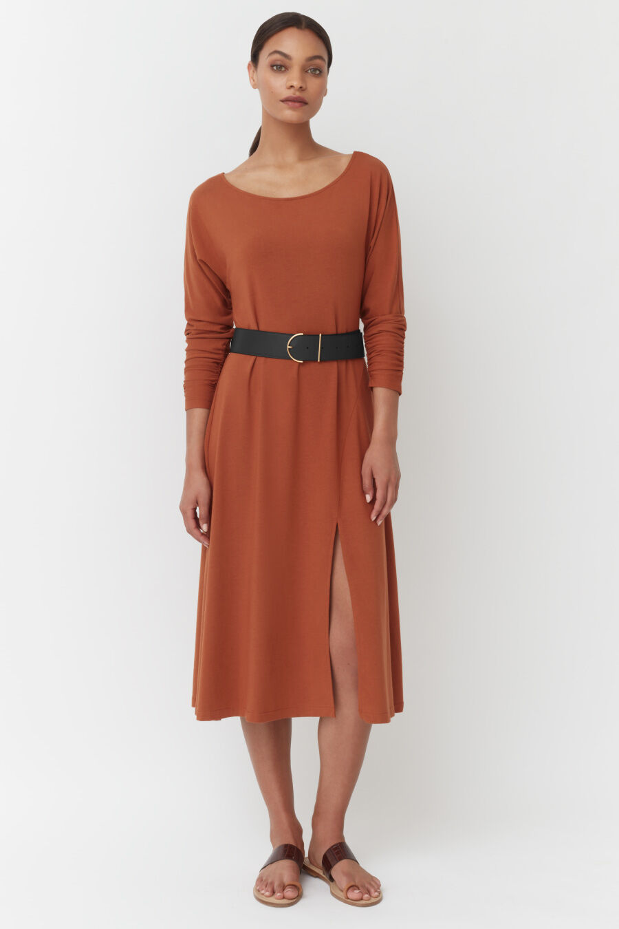 Woman standing in a belted knee-length dress and sandals.