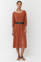 Woman standing in a belted knee-length dress and sandals.
