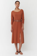 Woman standing in belted dress and sandals.