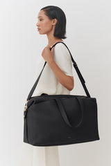 Woman standing side profile carrying a large shoulder bag.