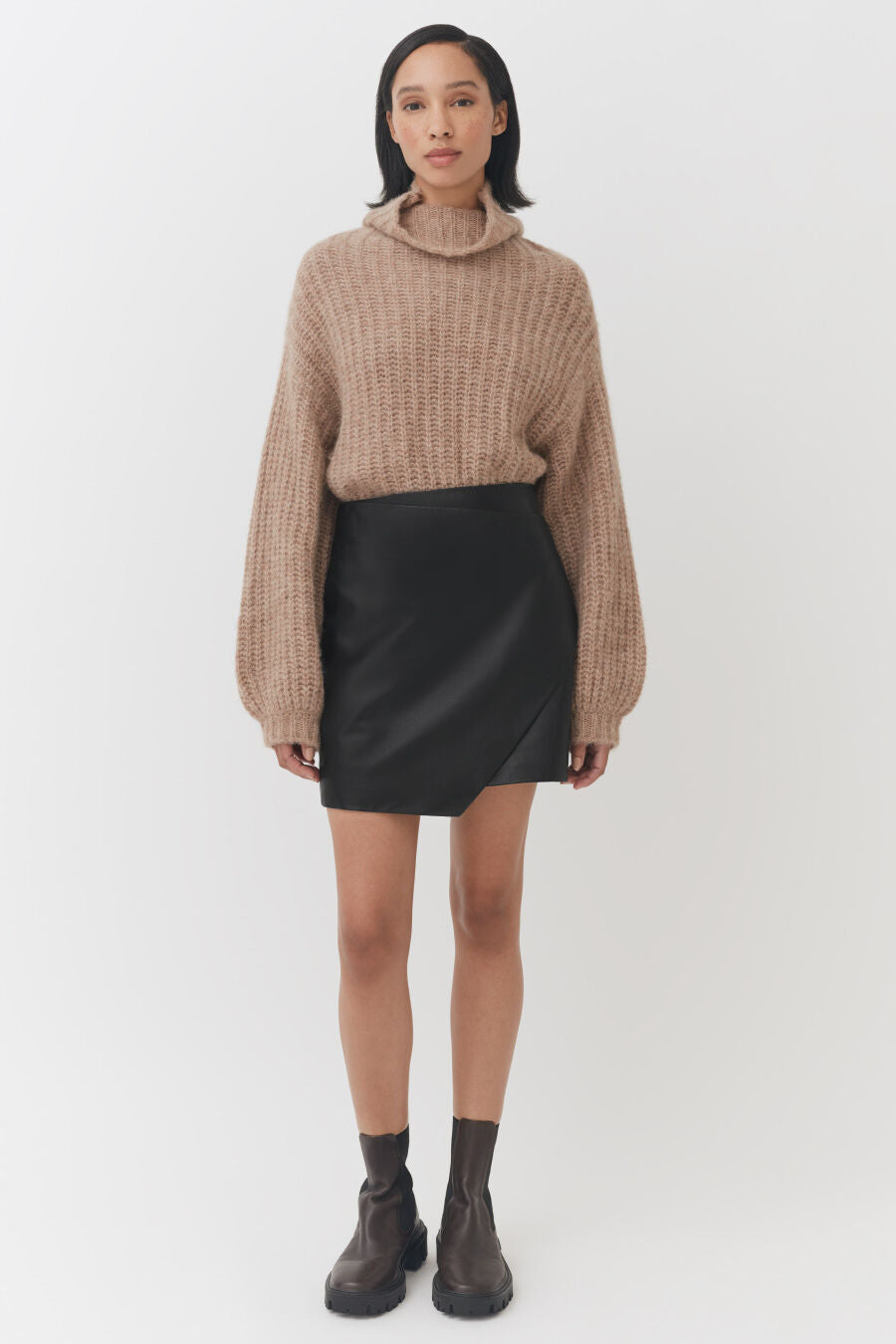 Woman standing in a sweater, skirt, and boots.