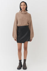 Woman standing in a sweater, skirt, and boots.