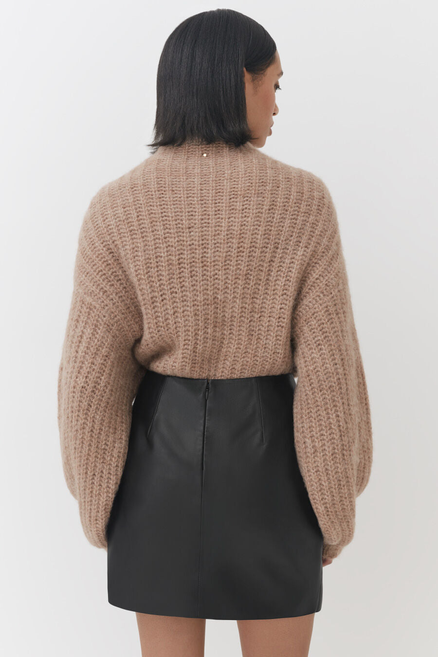 Woman wearing a sweater and skirt, viewed from behind.