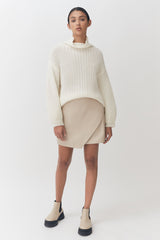 Woman standing in a sweater and skirt with ankle boots.