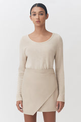 Woman standing in sweater and asymmetrical skirt facing the camera.