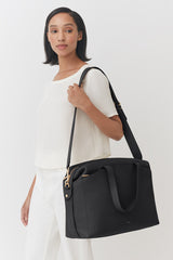 Woman carrying a large shoulder bag, standing indoors.