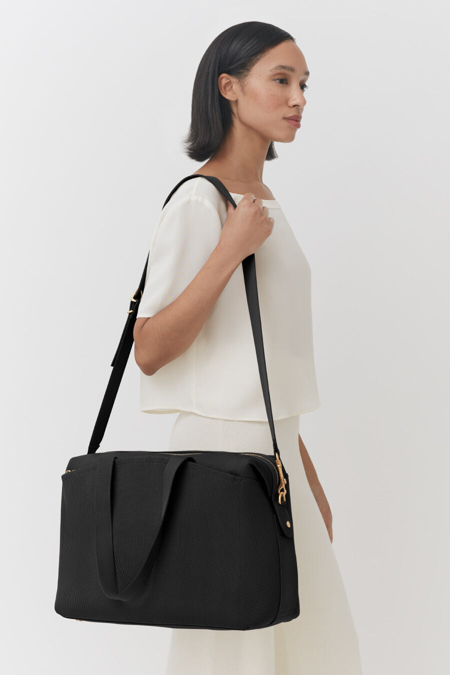 Woman standing sideways carrying a large shoulder bag.