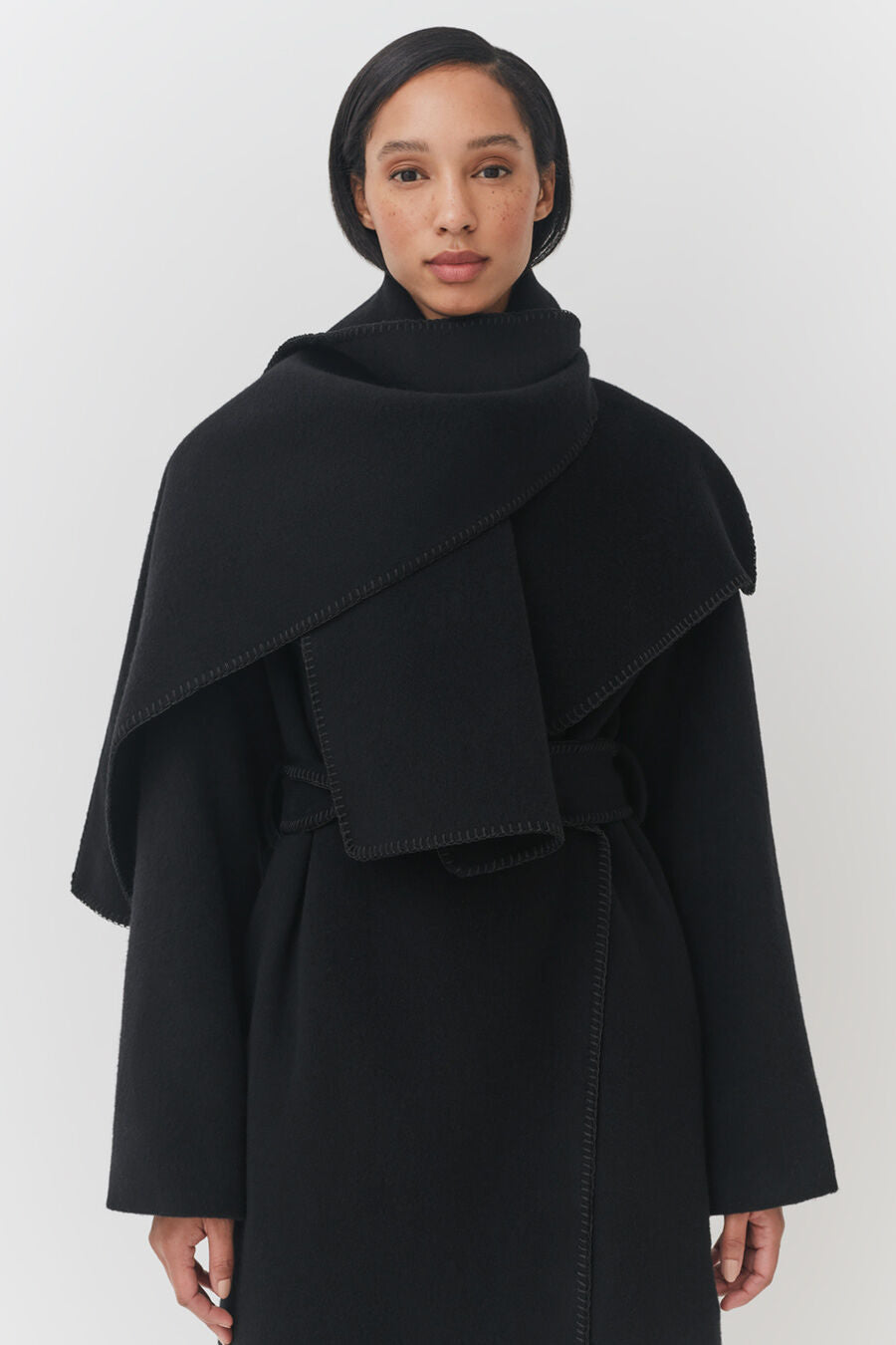 Woman in a turtleneck and layered coat standing against a plain background.