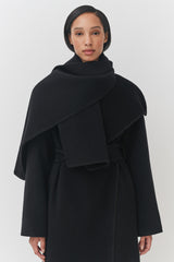 Woman in a turtleneck and layered coat standing against a plain background.