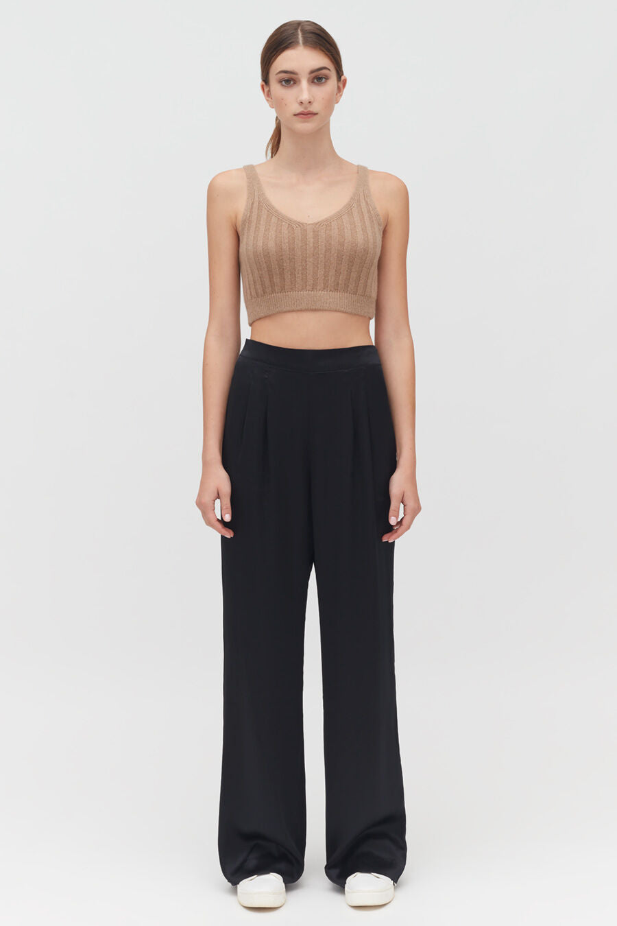 Woman standing in sleeveless top and trousers, facing forward.