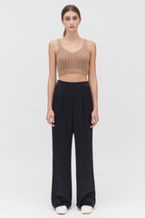 Woman standing in sleeveless top and trousers, facing forward.