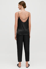 Woman from behind, wearing a strappy top and trousers, standing.