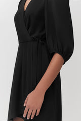 Person in a dress with a tied waist detail and puffed sleeves.