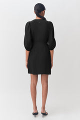 Woman seen from behind wearing a dress with puffy sleeves and standing.