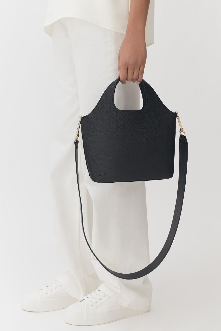 Person holding a handbag with a shoulder strap.