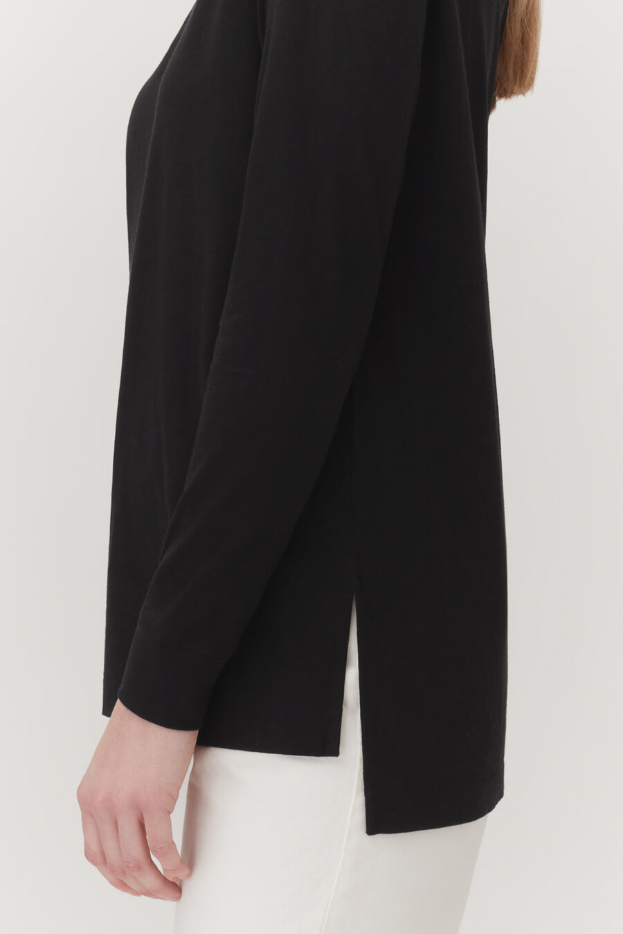 Woman wearing a long sleeve top and pants, partial side view.