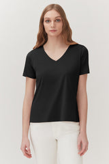 Woman in V-neck T-shirt standing against a plain background.