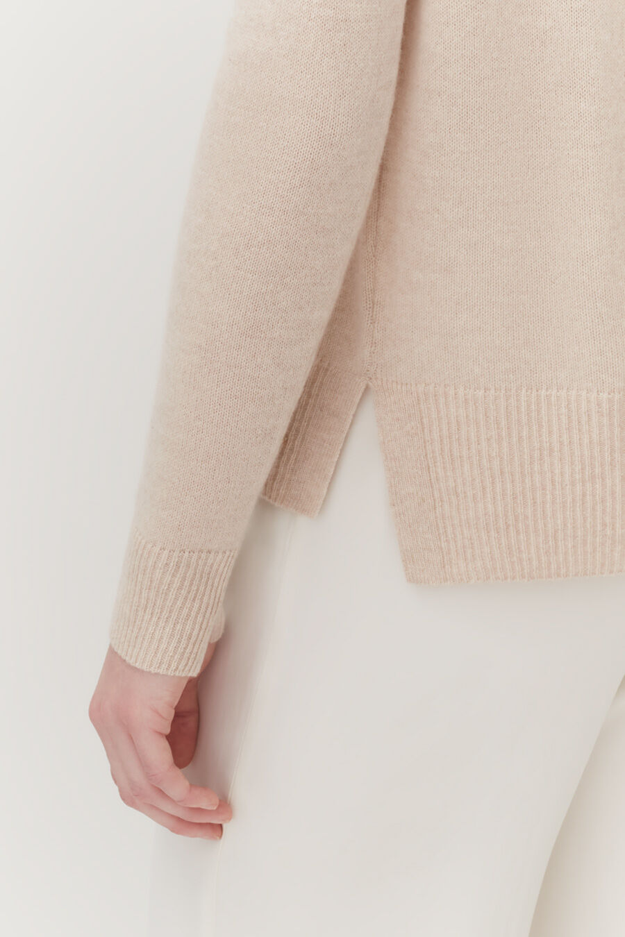 Close-up of a person's arm in a sweater leaning against a wall