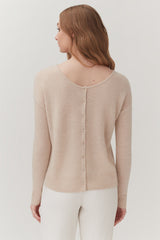 Woman in a sweater with buttons down the back, standing, viewed from the rear.