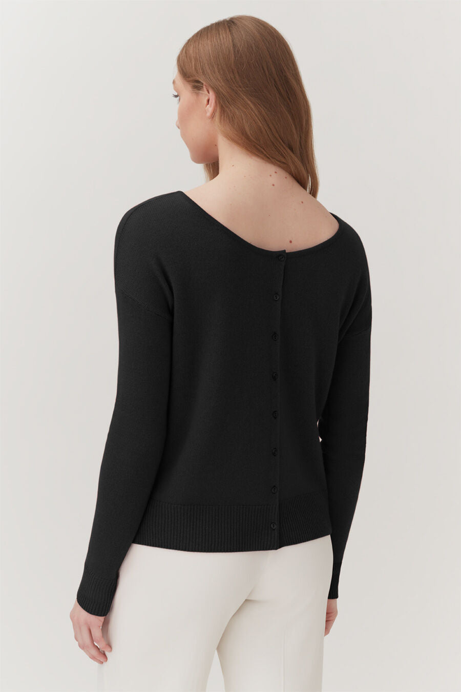 Woman from behind wearing a buttoned sweater and pants.
