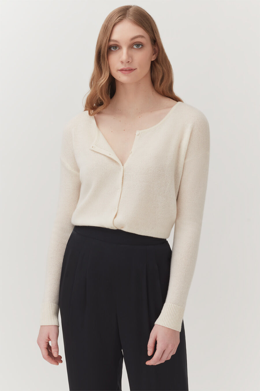 Single-Origin Cashmere Cardigan Woman wearing a buttoned sweater and trousers standing straight.