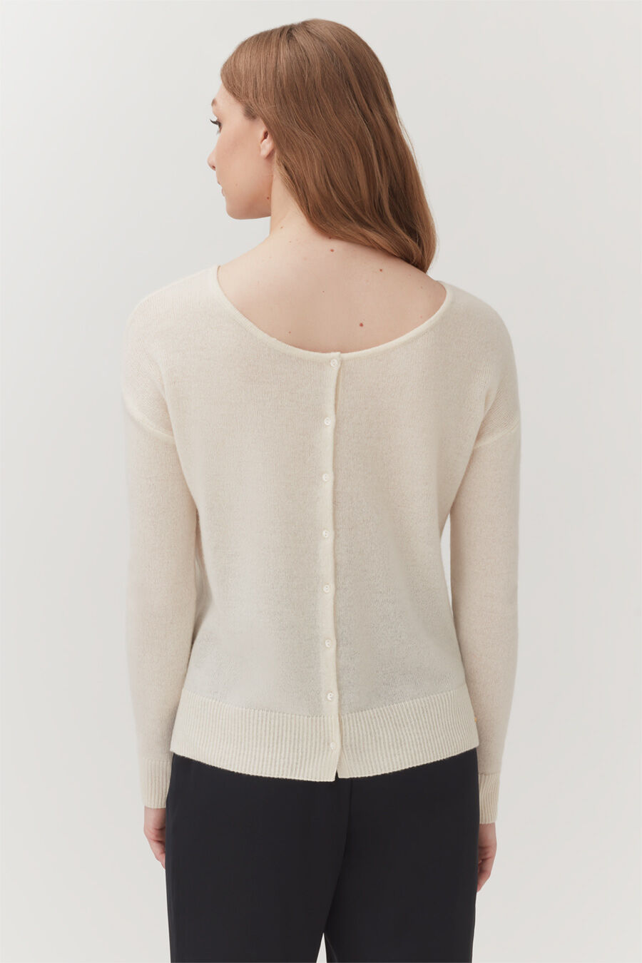 Single-Origin Cashmere Cardigan Woman wearing a cardigan with buttons on the back, standing.