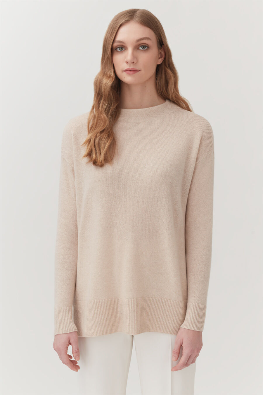 Single-Origin Cashmere Funnel Neck Sweater Woman standing in a sweater and pants, looking at the camera.