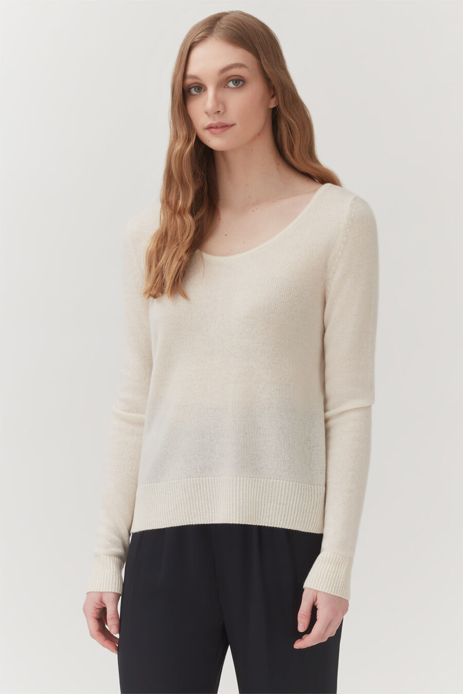 Single-Origin Cashmere Scoop Neck Sweater Woman in a long sleeve top and trousers standing indoors.