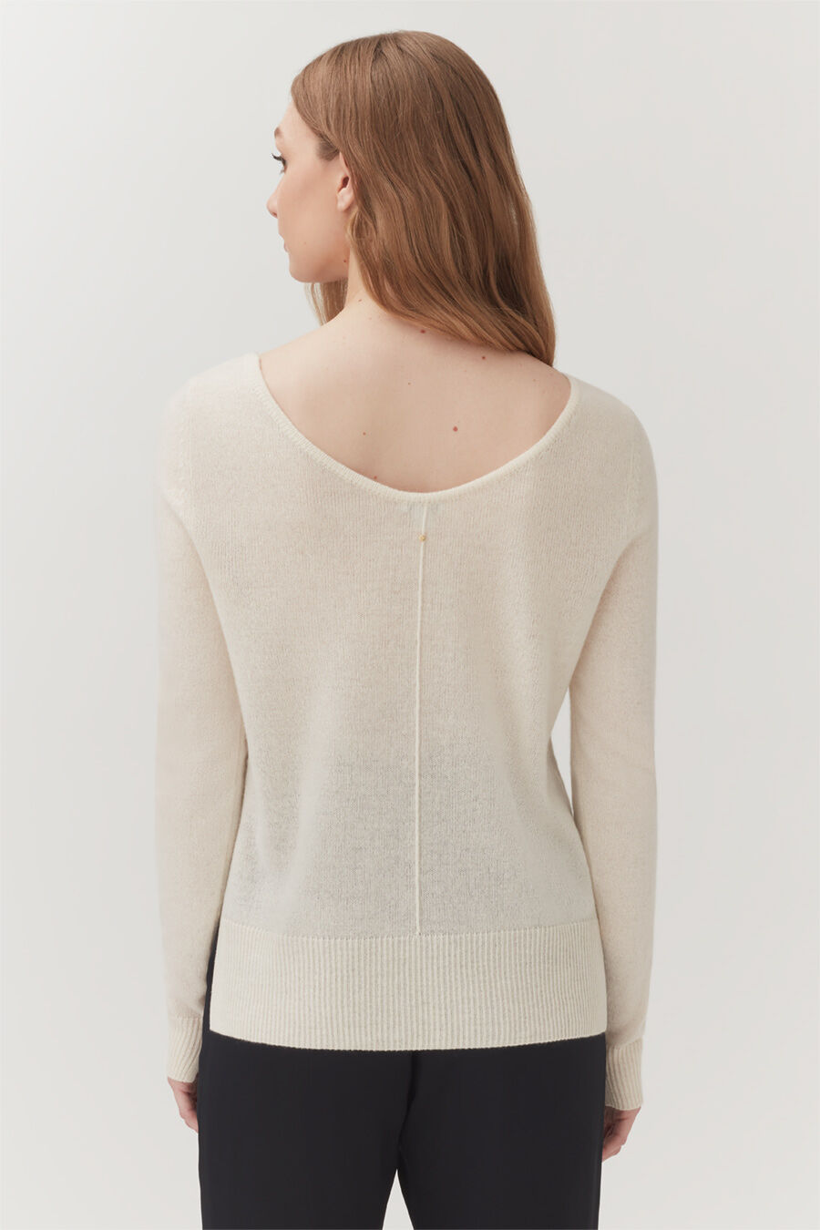 Single-Origin Cashmere Scoop Neck Sweater Woman standing, seen from behind, wearing a sweater with a zipper down the back.
