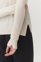 Person holding their own elbow, dressed in a sweater and pants.