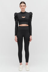 Woman in unique top and leggings standing against a plain background